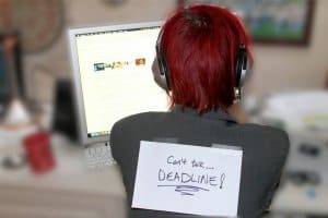 Woman sitting in front of a computer with a sign on her back: Can't talk....Deadline!