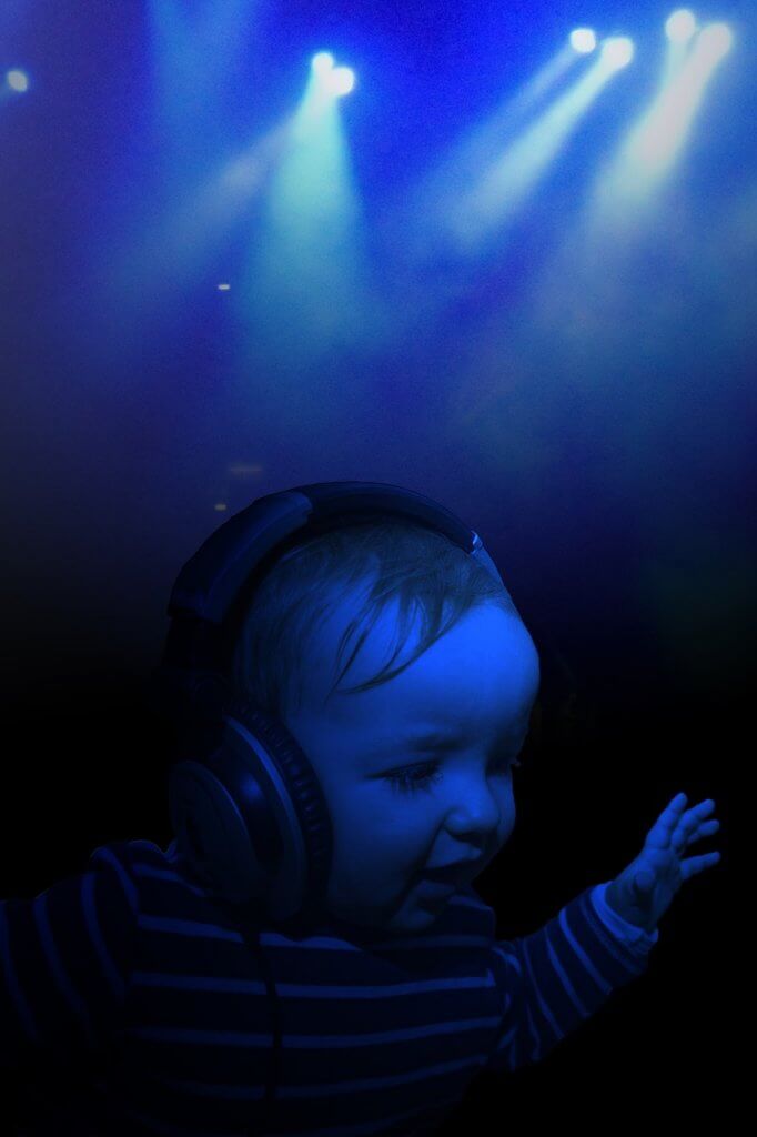 A child wearing large headphones is illuminated by blue stage lights in a dark environment.