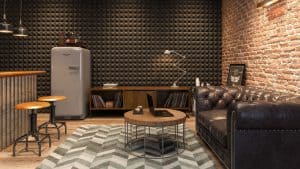 A cozy room with a leather couch, a round wooden coffee table with a laptop, a vintage refrigerator, bar stools, a zigzag rug, vinyl records, and industrial-style decor.