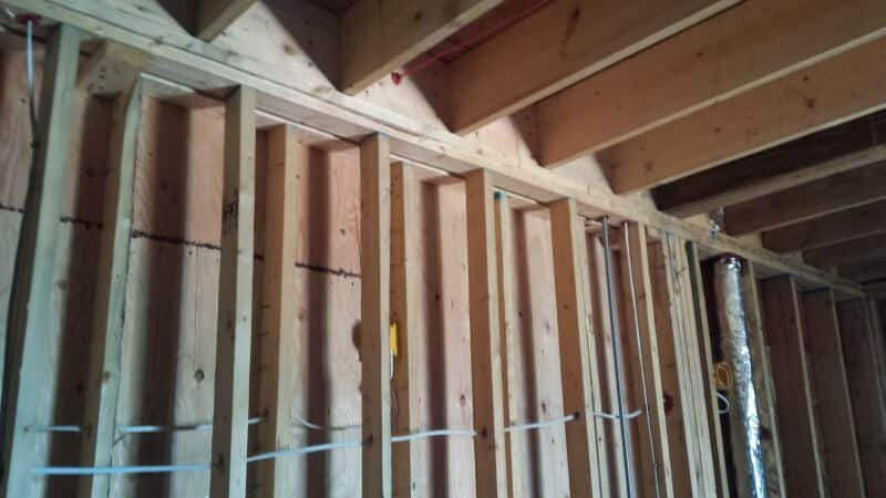 Wood framing and exposed insulation of an unfinished wall with visible electrical wiring within the construction area.